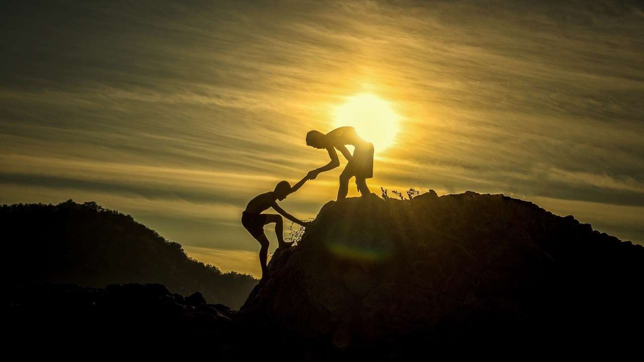 Une personne aidant un indivdu à grimper sur un sommet